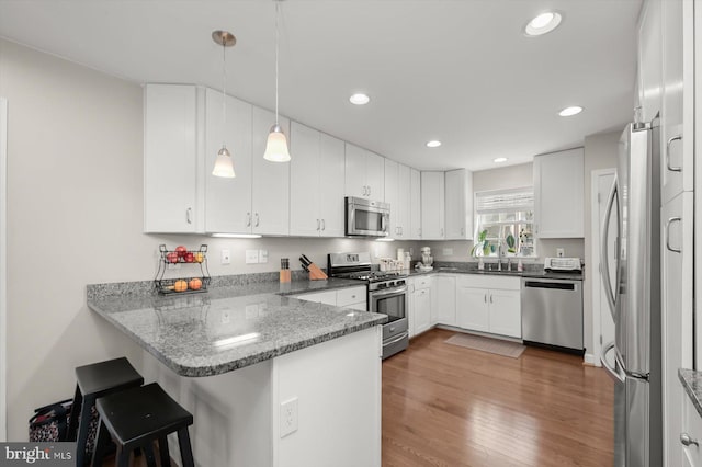 kitchen with wood finished floors, stainless steel appliances, a peninsula, white cabinets, and hanging light fixtures