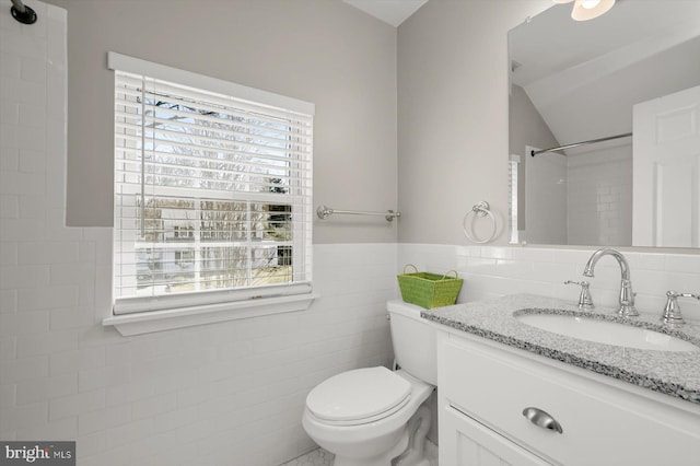 full bathroom featuring toilet, tile walls, wainscoting, vanity, and vaulted ceiling