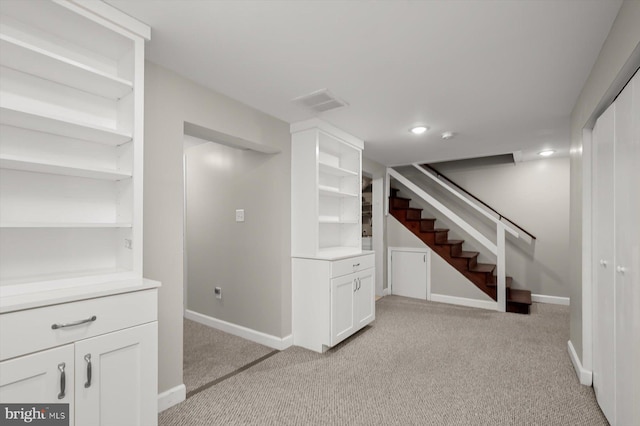 finished below grade area with visible vents, stairway, light colored carpet, and baseboards