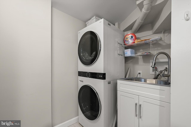 clothes washing area with cabinet space, stacked washing maching and dryer, baseboards, and a sink