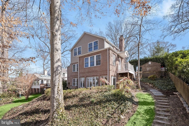 view of side of home with stairway, fence, a wooden deck, a chimney, and brick siding