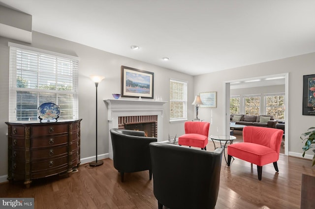 living room featuring a brick fireplace, baseboards, and wood finished floors