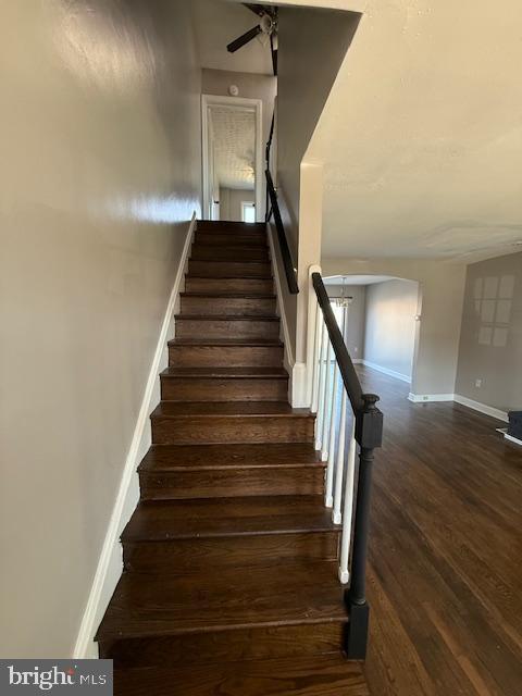 stairway with arched walkways, baseboards, a ceiling fan, and wood finished floors