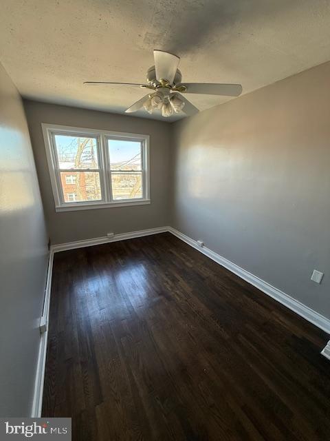 unfurnished room featuring dark wood finished floors, a textured ceiling, a ceiling fan, and baseboards