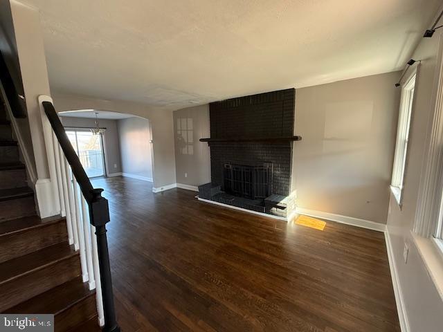 unfurnished living room featuring stairway, wood finished floors, baseboards, a fireplace, and arched walkways