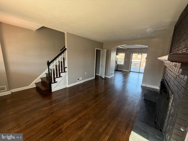 unfurnished living room featuring dark wood finished floors, stairway, arched walkways, a fireplace, and baseboards