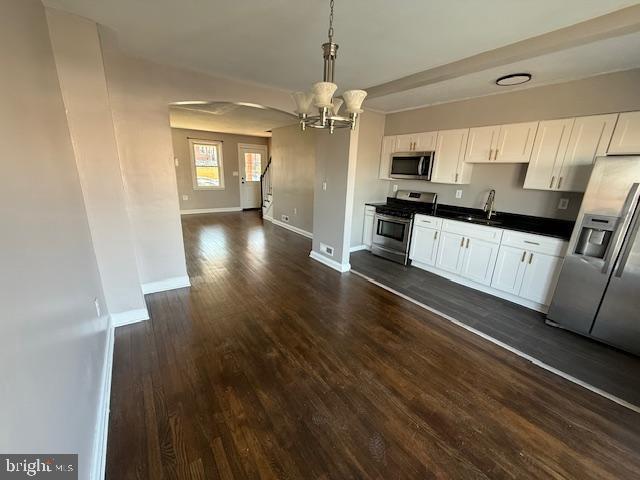 kitchen with dark countertops, dark wood finished floors, stainless steel appliances, white cabinetry, and a sink