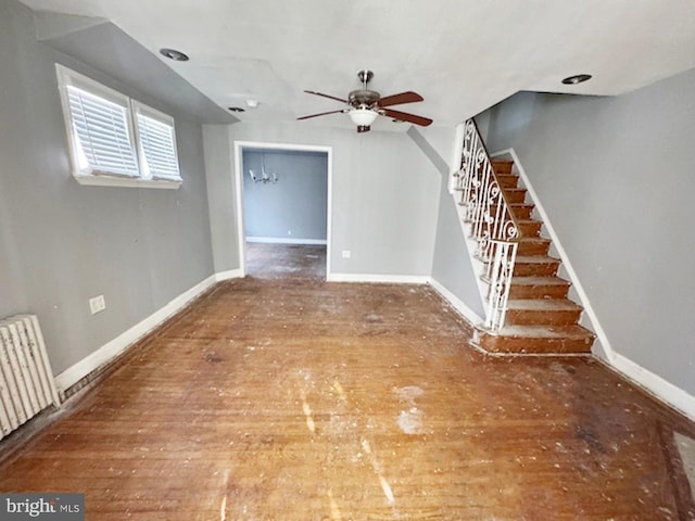 unfurnished living room featuring stairway, wood-type flooring, baseboards, and radiator heating unit