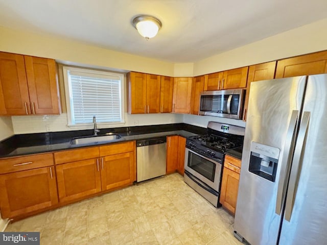 kitchen featuring dark countertops, brown cabinetry, appliances with stainless steel finishes, and a sink