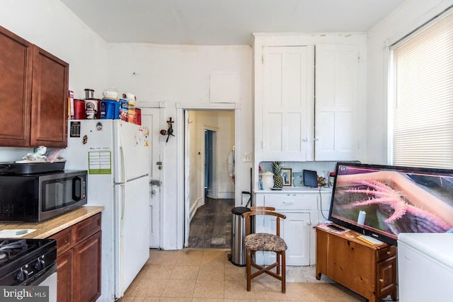 kitchen featuring freestanding refrigerator, stainless steel microwave, gas range, and light countertops