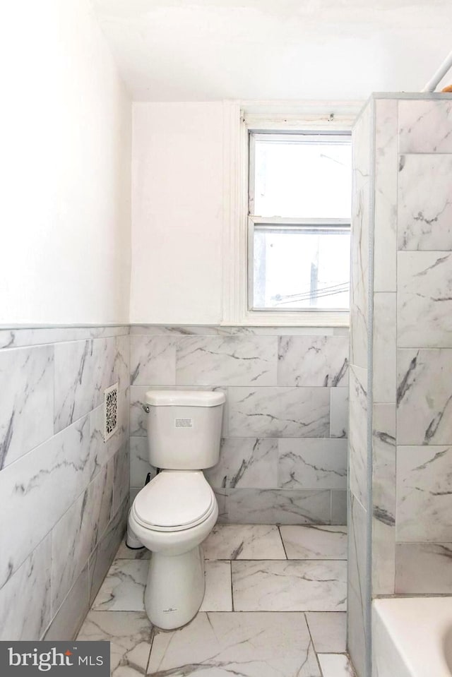 bathroom with a wainscoted wall, toilet, marble finish floor, a tub to relax in, and a shower