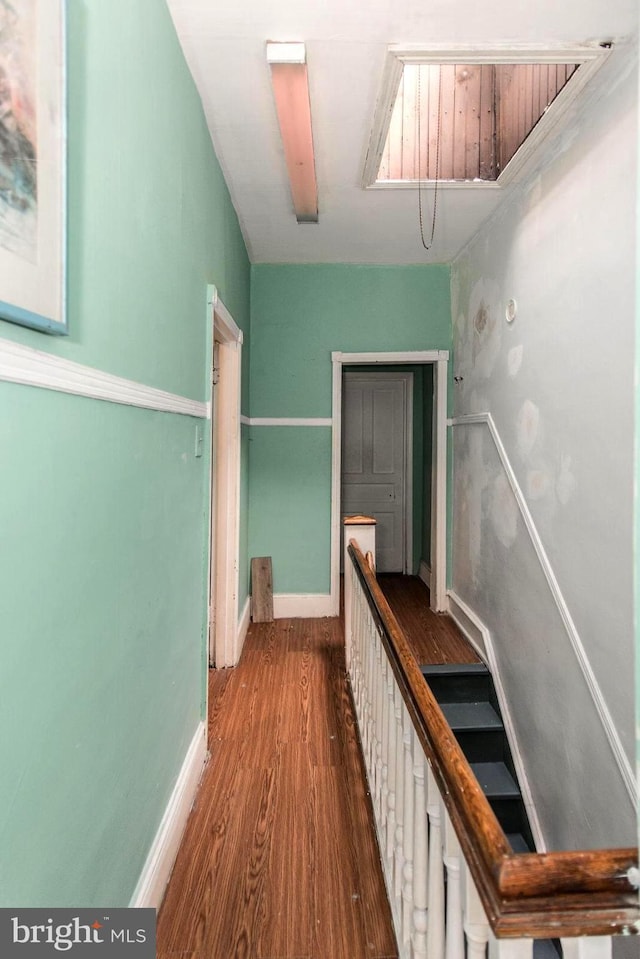 hall featuring an upstairs landing, baseboards, and wood finished floors