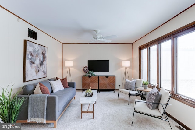 carpeted living area with visible vents, baseboards, crown molding, and a ceiling fan