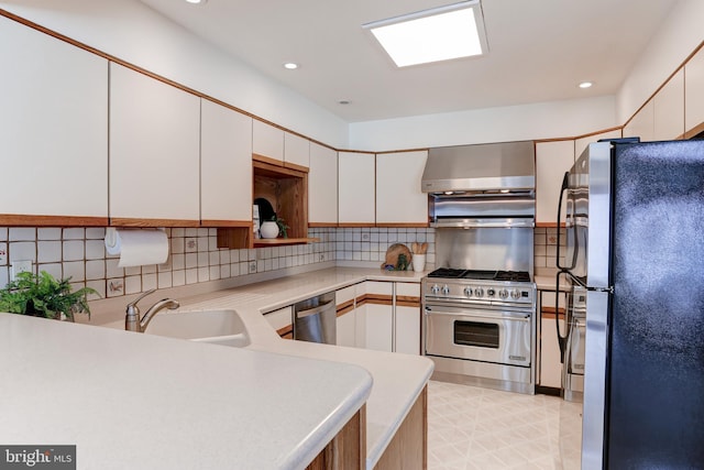 kitchen featuring backsplash, wall chimney range hood, light countertops, stainless steel appliances, and a sink