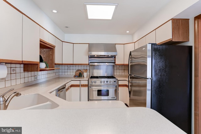 kitchen with a sink, light countertops, wall chimney exhaust hood, and stainless steel appliances