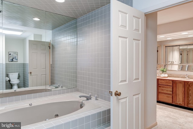 bathroom with vanity, tile walls, toilet, and a tub with jets