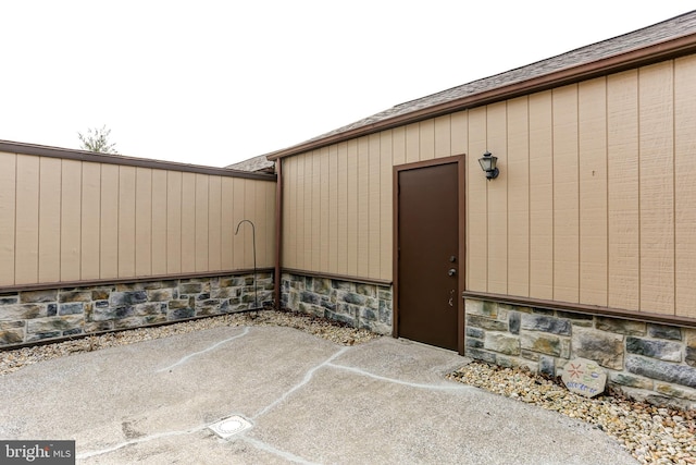 property entrance featuring stone siding, roof with shingles, and a patio