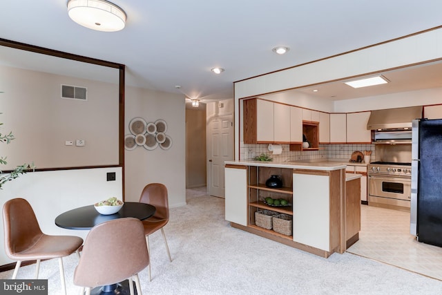 kitchen featuring visible vents, light countertops, light carpet, stainless steel appliances, and wall chimney exhaust hood