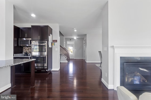 kitchen with backsplash, dark wood-type flooring, baseboards, light stone counters, and appliances with stainless steel finishes