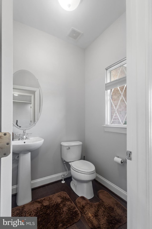 half bath featuring wood finished floors, baseboards, visible vents, a sink, and toilet