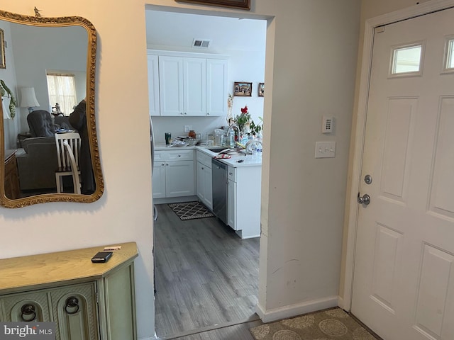 kitchen with wood finished floors, visible vents, white cabinetry, light countertops, and stainless steel dishwasher