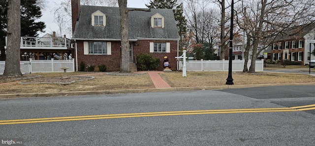 view of front of home with fence, brick siding, roof with shingles, and a chimney