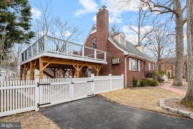 view of side of home with a gate, aphalt driveway, fence, brick siding, and a chimney