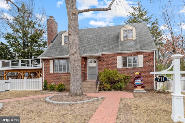 view of front of house featuring brick siding, roof with shingles, a chimney, and fence