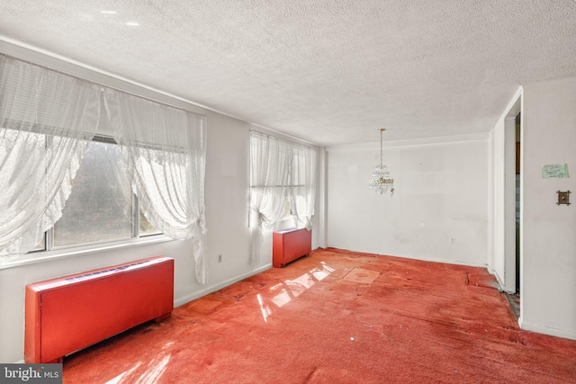 carpeted spare room with a textured ceiling, an inviting chandelier, and radiator heating unit