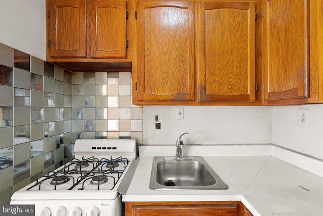 kitchen with brown cabinets, white gas stove, a sink, backsplash, and light countertops