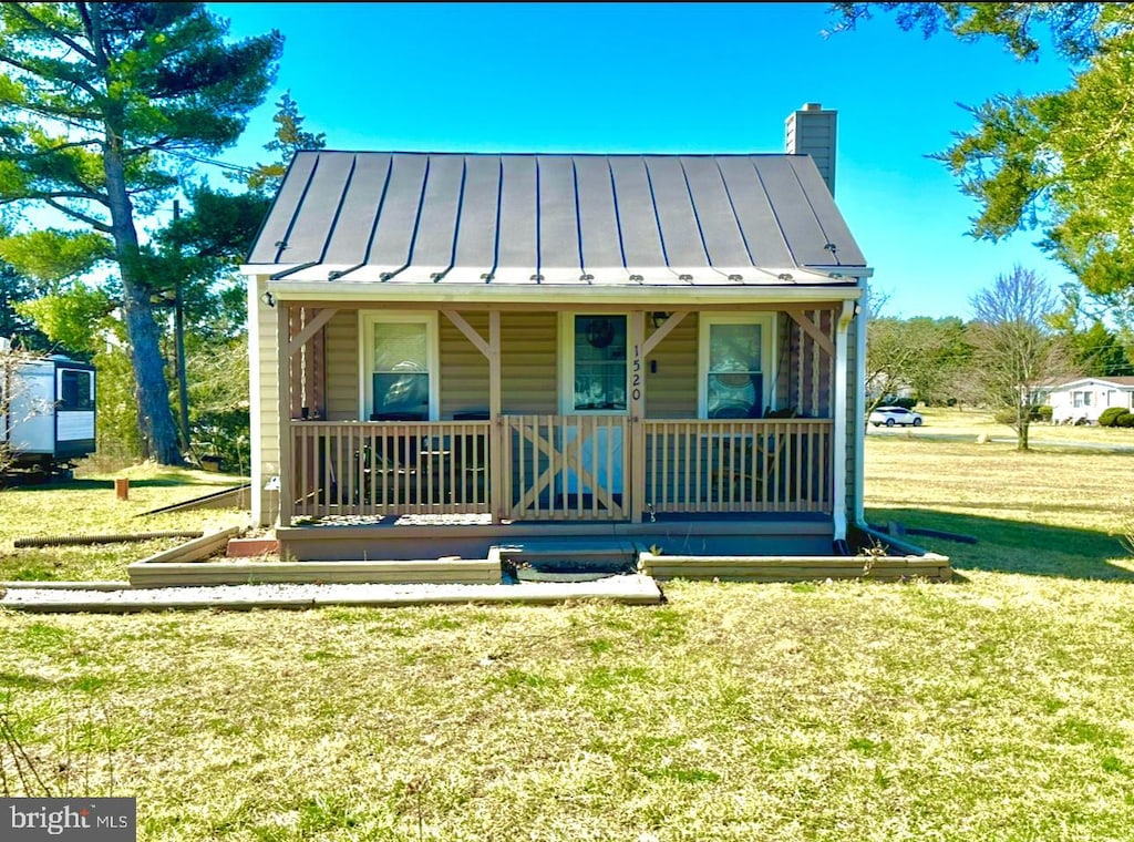 bungalow-style house with a front lawn, a porch, a chimney, metal roof, and a standing seam roof