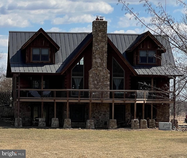 rear view of property with stone siding, a lawn, a chimney, and a standing seam roof