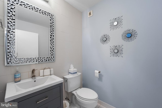 half bathroom featuring vanity, tile walls, toilet, and baseboards