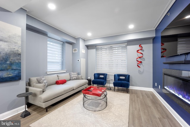 living area featuring baseboards, ornamental molding, recessed lighting, wood finished floors, and a glass covered fireplace