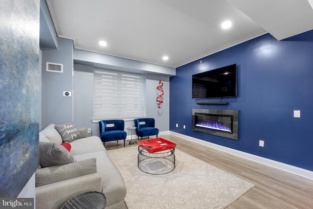 living area featuring visible vents, a glass covered fireplace, wood finished floors, crown molding, and baseboards