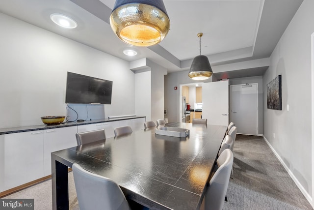 carpeted dining space featuring baseboards and a tray ceiling