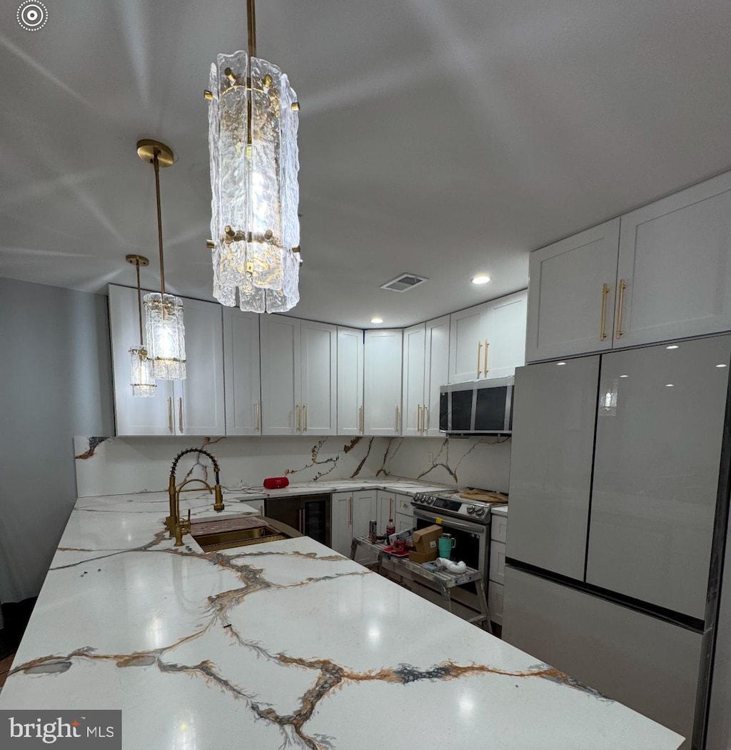 kitchen featuring light stone counters, a sink, stainless steel appliances, white cabinets, and pendant lighting