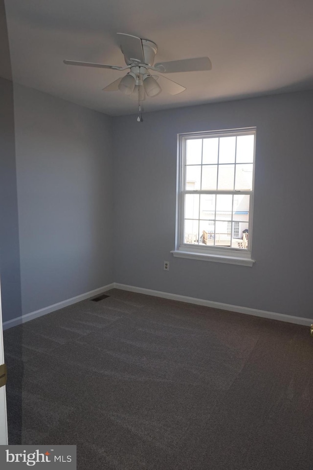 spare room with dark carpet, baseboards, and ceiling fan