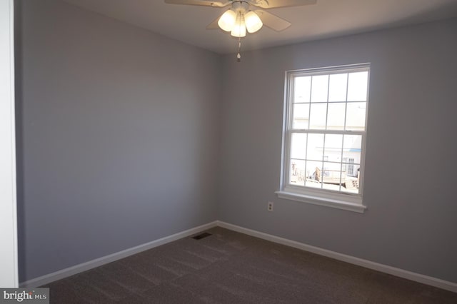 empty room with dark colored carpet, baseboards, plenty of natural light, and visible vents