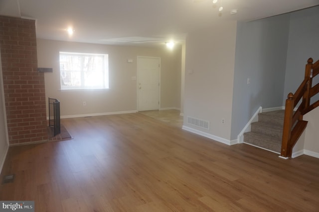 unfurnished living room with stairs, wood finished floors, visible vents, and baseboards