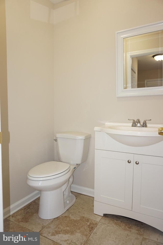 half bathroom with vanity, toilet, and baseboards