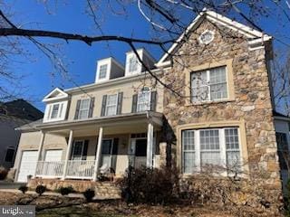 view of front of home featuring a garage, covered porch, and stone siding