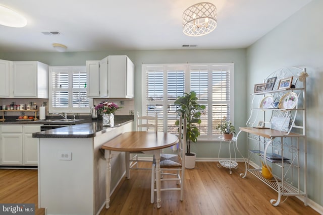 kitchen featuring a sink, dark countertops, backsplash, light wood-style floors, and white cabinets