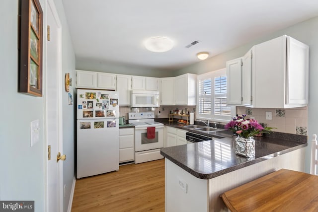 kitchen featuring a sink, white appliances, dark countertops, and a peninsula