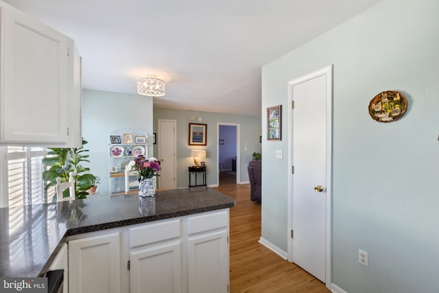 kitchen with baseboards, a peninsula, light wood-style floors, white cabinetry, and dark countertops