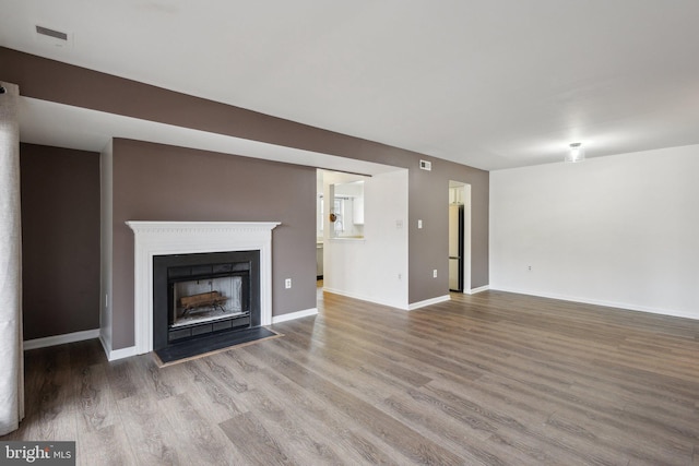 unfurnished living room featuring a fireplace with flush hearth, wood finished floors, visible vents, and baseboards