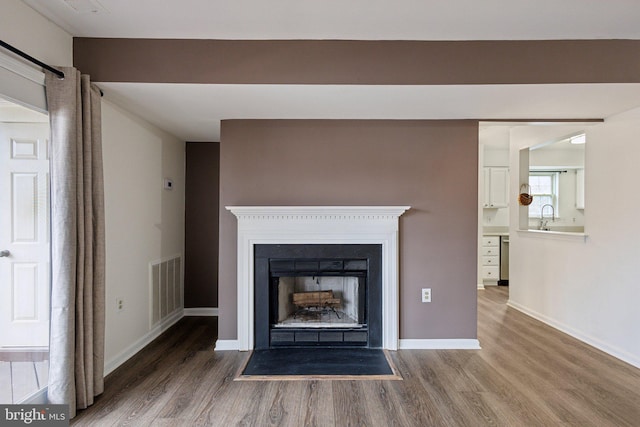 interior details featuring a sink, visible vents, baseboards, and wood finished floors