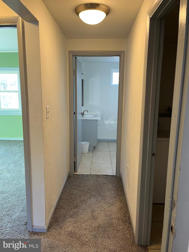 hallway with light carpet, baseboards, and a textured wall