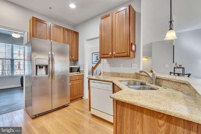 kitchen with light wood finished floors, pendant lighting, light stone counters, appliances with stainless steel finishes, and a sink