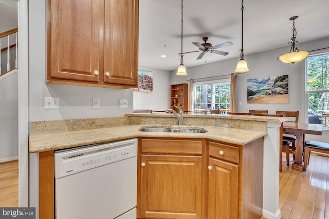 kitchen with light wood-type flooring, a sink, a peninsula, white dishwasher, and light stone countertops